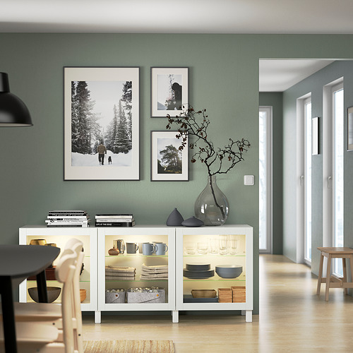 Comedor moderno con aparador blanco BESTÅ, puertas de cristal, mesa y fotos.