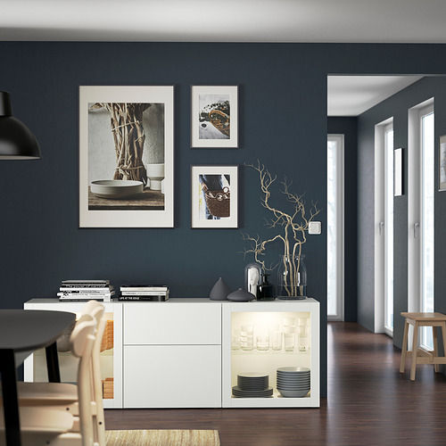 Comedor moderno con aparador BESTÅ, cristalería, platos. Arte minimalista, suelo de madera oscura, muebles ligeros.