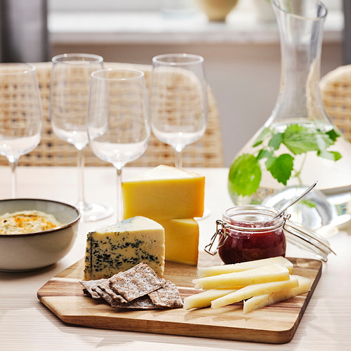 La tabla de cortar de madera contiene queso, cuchillo y galletas saladas. Cuatro copas de vino se alinean en la parte posterior.