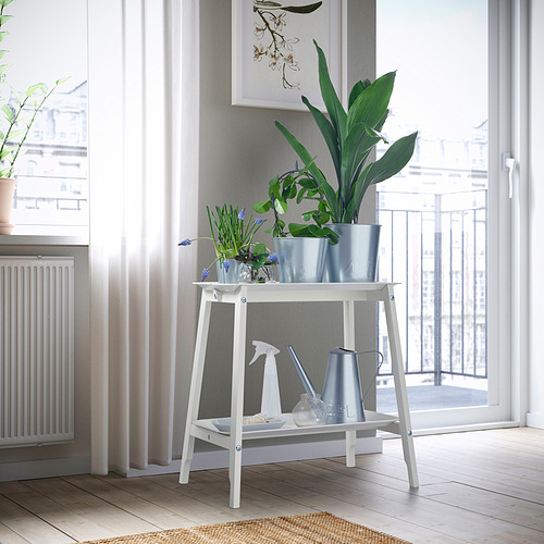 Soporte de plantas blancas ALPVIDE cerca de la ventana con grandes plantas de interior, bandeja pequeña, regadera y botella rociadora.