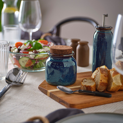 La jarra azul BRUGDHAJ en una mesa rústica, más pequeña que una copa de vino, contiene especias o salsas.