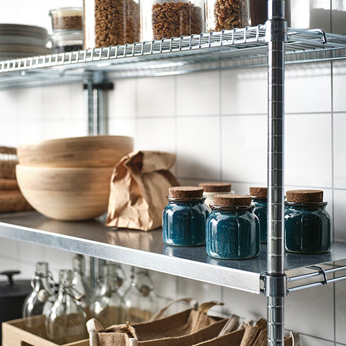 Estanterías metálicas de cocina que almacenan tarros de cristal con tapas de corcho y cuencos de madera.