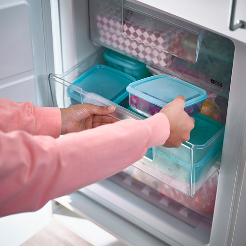 Persona colocando un recipiente azul en una nevera, sosteniendo más recipientes, manteniendo las sobras frescas y organizadas.