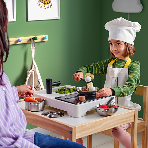 Niño con gorro de chef cocina en estufa de juguete con la ayuda de un adulto.