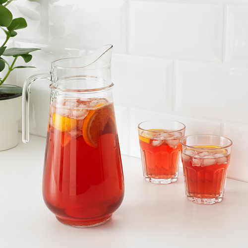 Jarra y vasos rellenos de bebida helada roja, adornados con rodajas de naranja. Un mango para facilitar el agarre y un pico para verter.