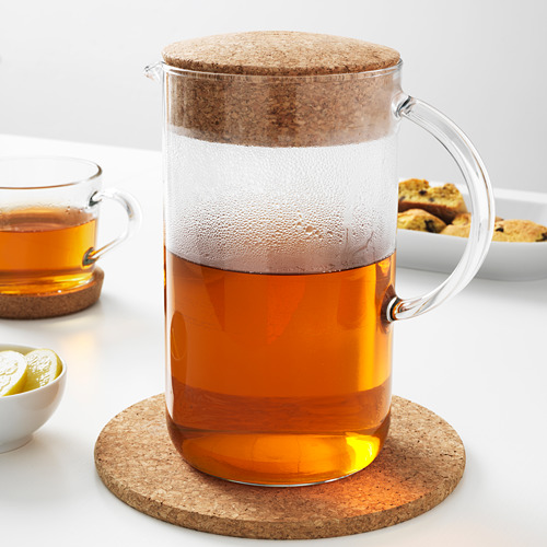 Tetera de vidrio con tapa de corcho, que contiene té empapado, que descansa sobre un posavasos de corcho.