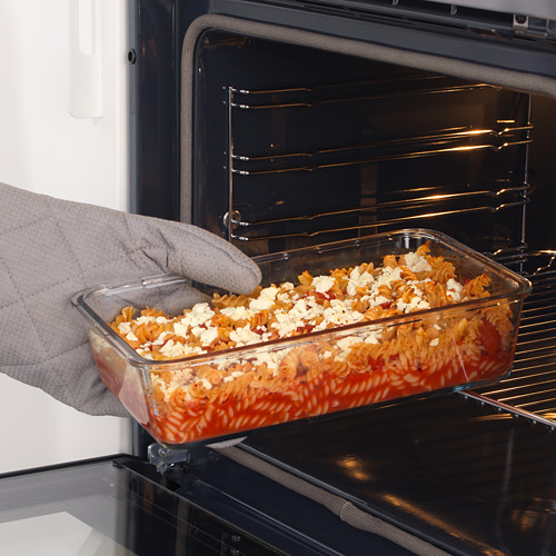 Persona colocando una fuente de vidrio para hornear, llena de pasta y queso en capas, en un horno.