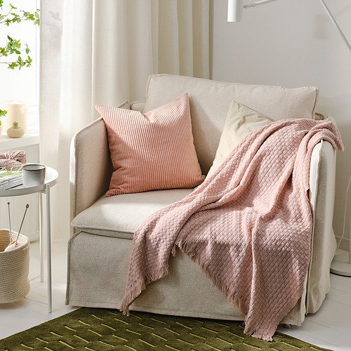 Sillón HORNMAL beige con manta y almohadas de color rosa claro en un acogedor espacio habitable.