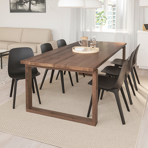 Comedor moderno con mesa de roble MÖRBYLÅNGA y sillas negras, alfombra beige, sofá, cortinas blancas, diseño minimalista.