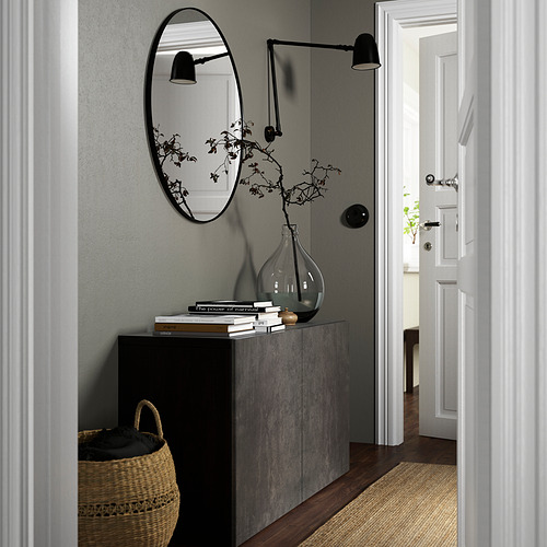 Pasillo moderno con aparador gris BESTÅ, espejo redondo, lámpara de pared, cesta de mimbre y planta seca.