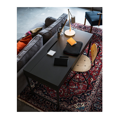 Oficina en casa moderna: silla ajustable, escritorio, alfombra colorida, papelería, lámpara, computadora portátil; Sofá con almohadas.