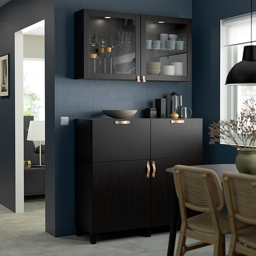Moderno mueble de almacenamiento gris BESTÅ con vitrinas, con tazas, platos y copas de vino en un comedor.