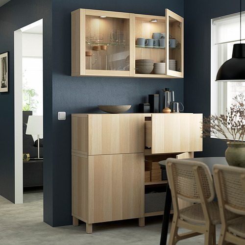 Light wood BESTÅ unit with glass doors and drawers against blue wall.