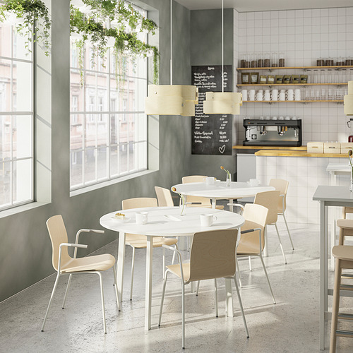 Cafetería moderna con mesas redondas MITTZON, sillas de madera clara, ventanas luminosas, plantas colgantes. Mesas pequeñas, con capacidad para cuatro personas cada una.