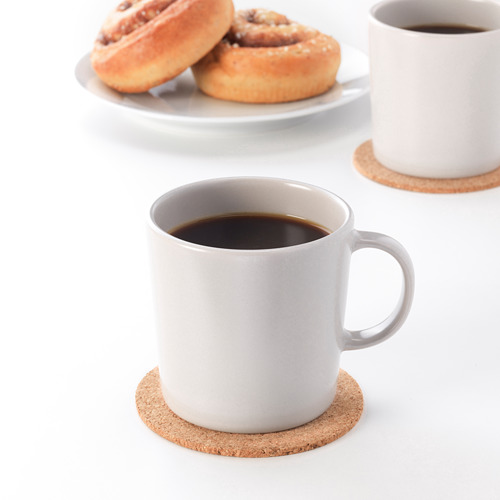 Dos tazas, una con café, en posavasos de corcho. Dos pasteles detrás. Mesa rústica con gres DINERA.
