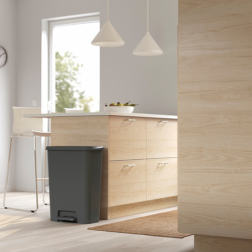 Cocina moderna con armarios de madera, papelera negra, cuenco de fruta.