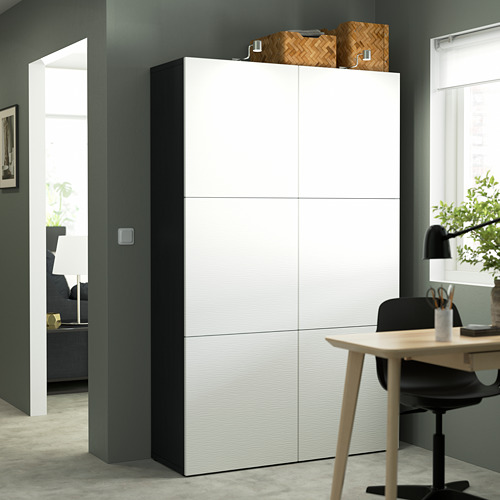 Gran armario de almacenamiento blanco BESTÅ contra una pared oscura, más alto que el escritorio y la silla cercanos.