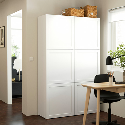 Mueble de almacenamiento blanco BESTÅ en la sala de estar, más alto que el escritorio adyacente, con cestas tejidas en la parte superior.