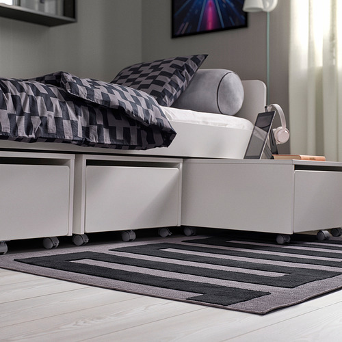 Dormitorio adolescente con alfombra BLÅSKATA, ropa de cama a juego, a rayas, suave, colocada debajo de la cama, suelo gris claro, muebles blancos.
