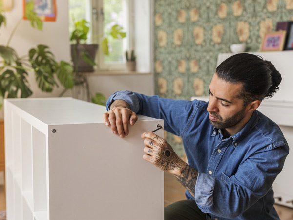 Man assembling a white shelving unit with an Allen key at home.