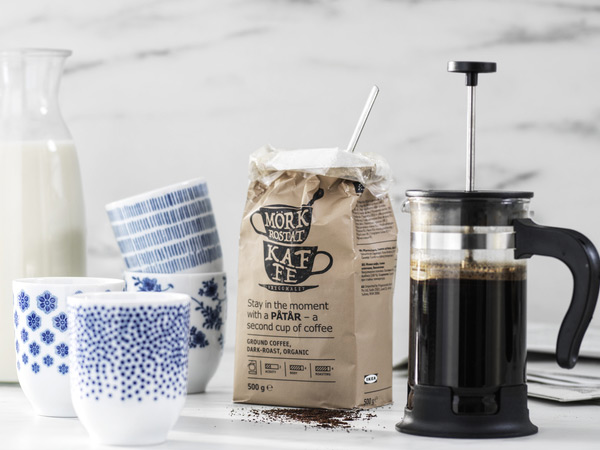 French press coffee maker next to a bag of ground coffee and cups.