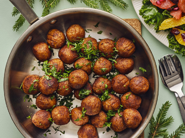 Golden meatballs topped with fresh parsley in a skillet beside a salad.