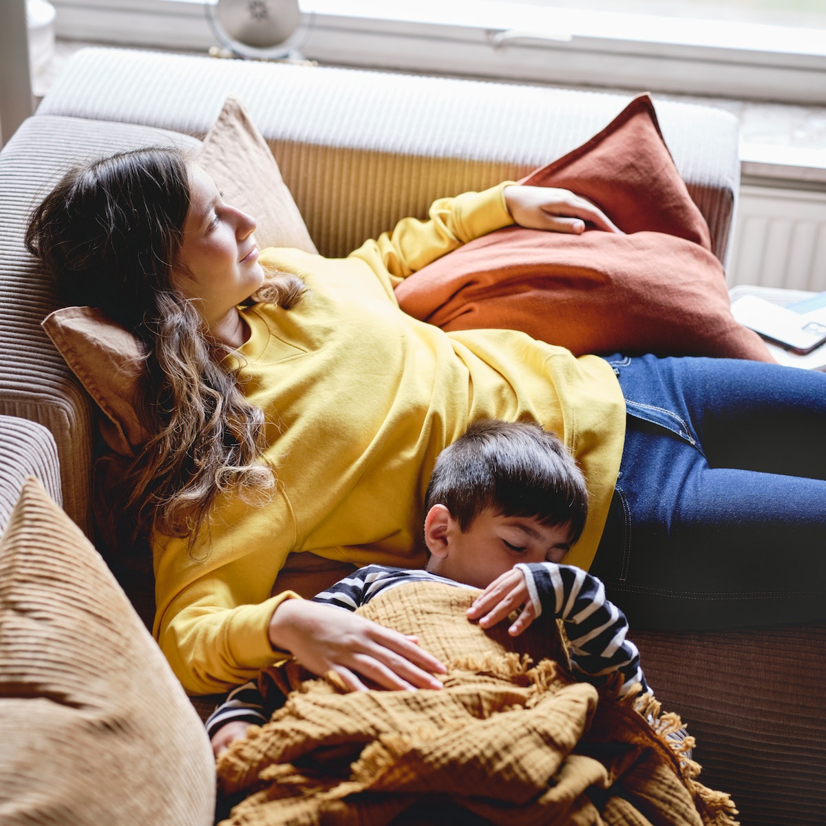 Madre descansando en el sofá mientras su hijo duerme.