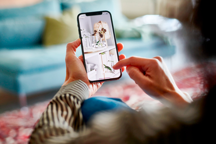 Person holding a smartphone to browse home decor photos while sitting indoors.