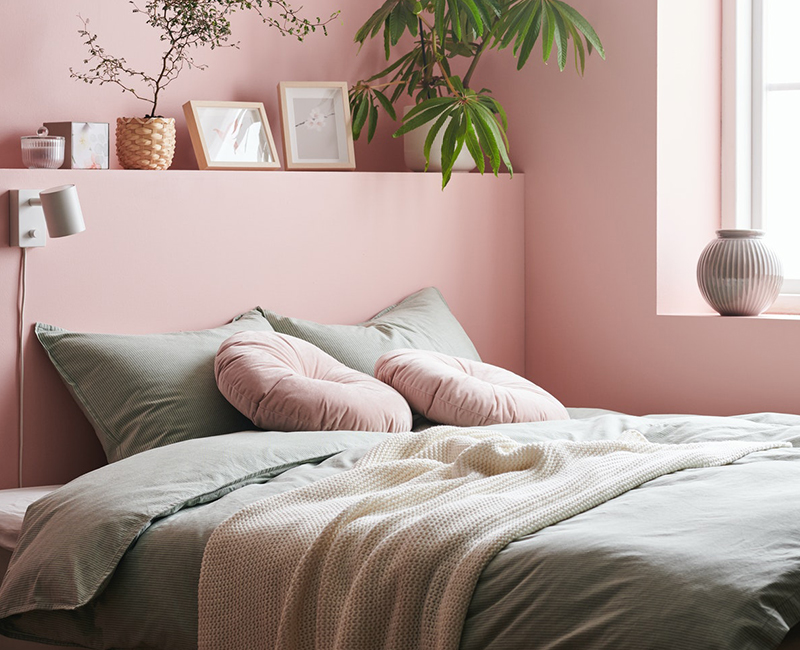  Dusty pink bedroom with green bedding, white knit throw, and two round pink cushions.