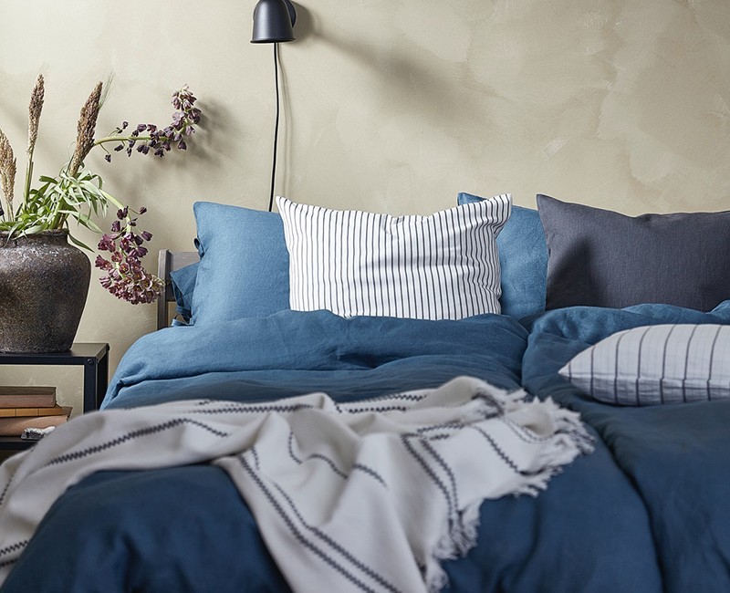  Blue linen bedding, striped pillow, white throw. Calm bedroom.