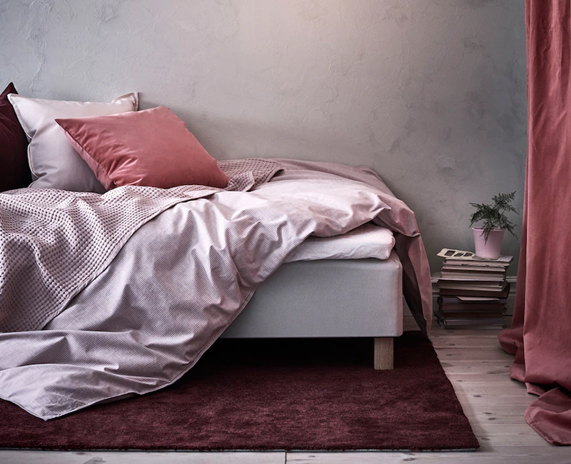 Soft pink bedding and a darker pink throw create a cozy bedroom. A burgundy rug and matching curtain add warmth.