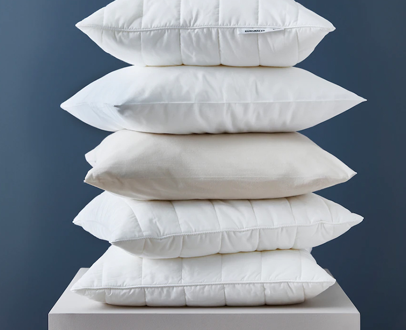 Stacked white and beige memory foam pillows create a soft, inviting look against a blue wall.