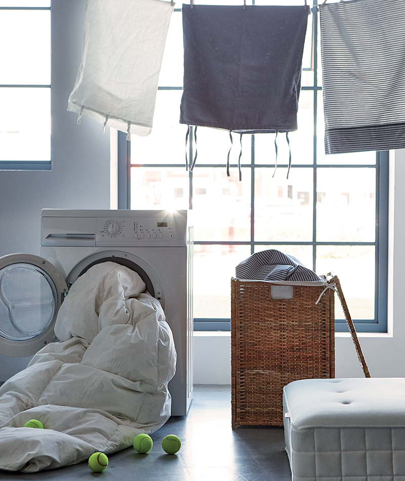 White washing machine with duvet, wicker basket, white ottoman, and laundry hanging. Functional utility.