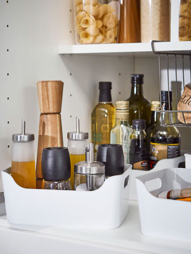 Kitchen shelf with spice containers, salt and pepper shakers, olive oil bottles in plastic box and rack