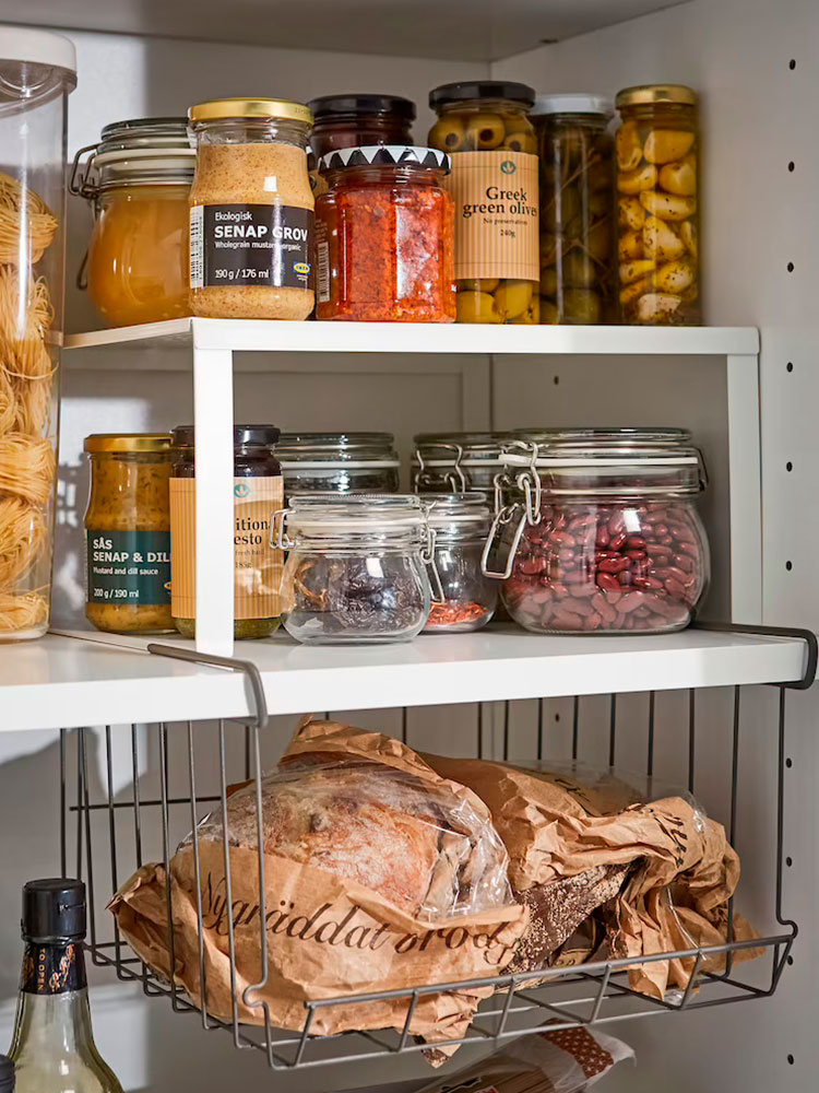 Upper pantry with spice jars on a small inner shelf and a wire basket below filled with cooking ingredients in a rustic kitchen setup