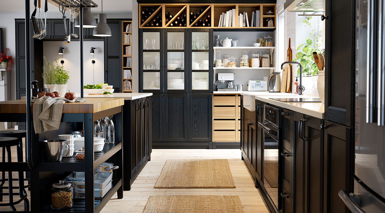 A well-lit kitchen with a VADHOLMA island, on the right a kitchen cabinet with a LAGAN induction cooktop, and in the background a kitchen shelving unit with doors and a VADHOLMA wine rack.