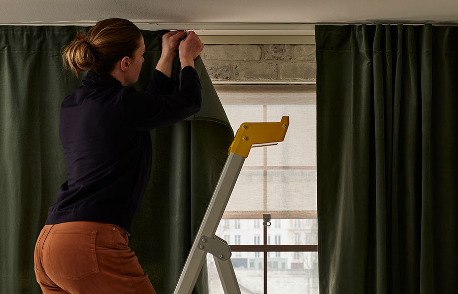 A woman hanging curtains on a VIDGA curtain set.