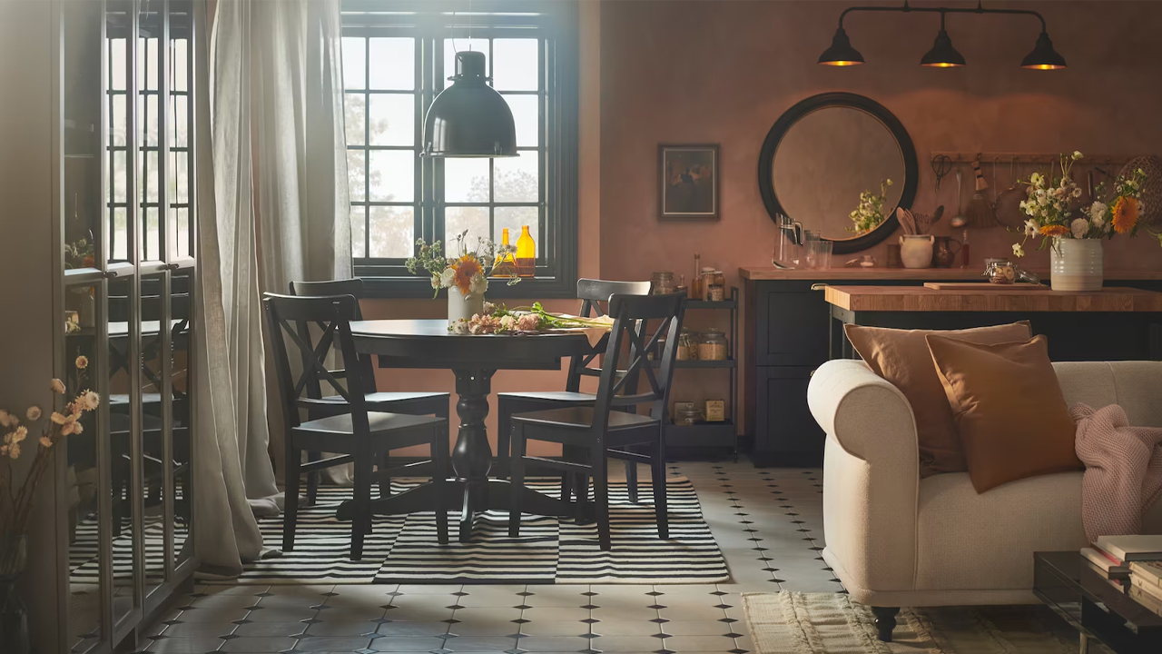 A neutral-toned living and dining area with a beige sofa, dark round table, and a mix of striped and plain rugs.