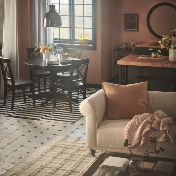 An earth-toned living and dining area with a white sofa, a black round table, and patterned rugs.