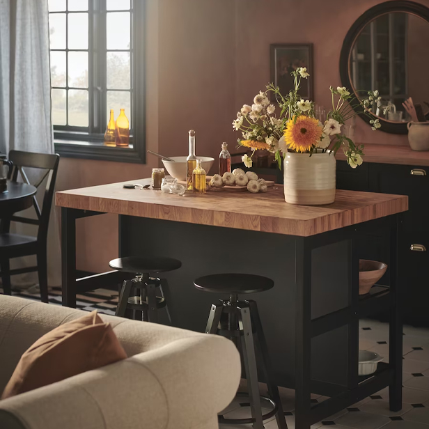 A kitchen island with a wooden top and black base, adorned with flowers and utensils, in a warm ambiance.