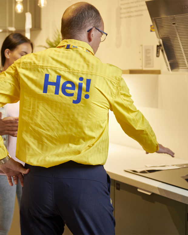 IKEA customer service person, from the back, dressed in yellow striped shirt with “hej” written on the back of the shirt.