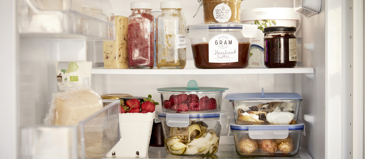 Organized fridge with jars, berries, and leftovers in reusable containers, promoting food preservation and less waste.