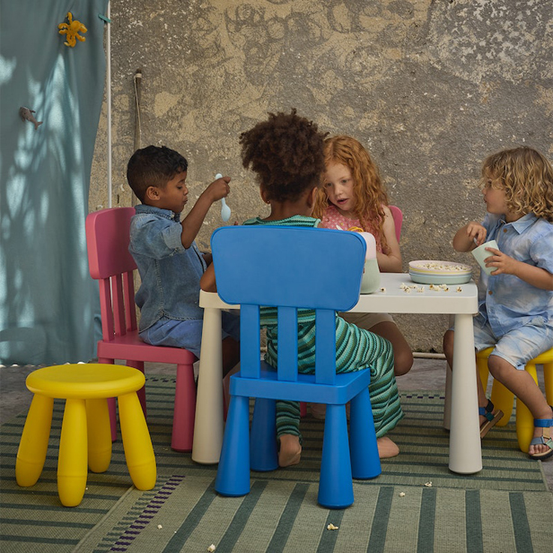 Back view of children seated around a small white table on pastel chairs