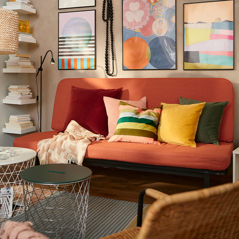 Colorful environment with a minimalist sofa with several multicolored cushions, 70's style, there is an open shelf of pine wood,