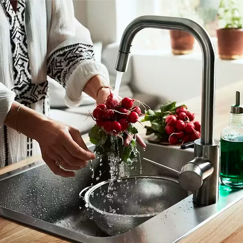 Hands rinsing radishes under a modern stainless steel faucet in a sink, with a colander and soap.