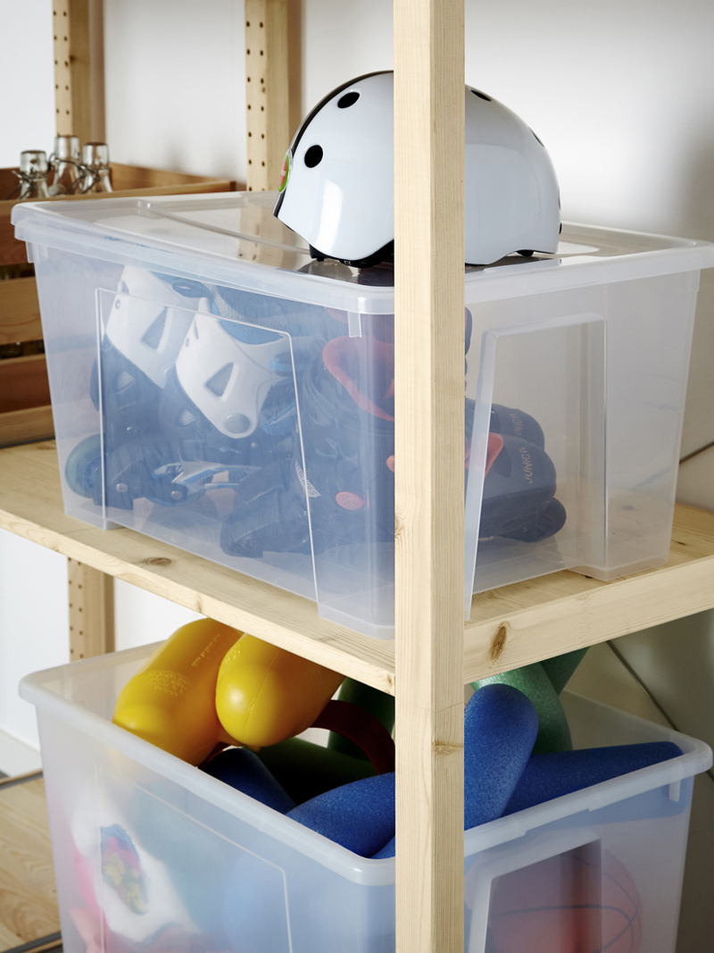 Light wood shelves with transparent boxes filled with sports items and games. A white helmet on top, creating an organized storage ambiance.