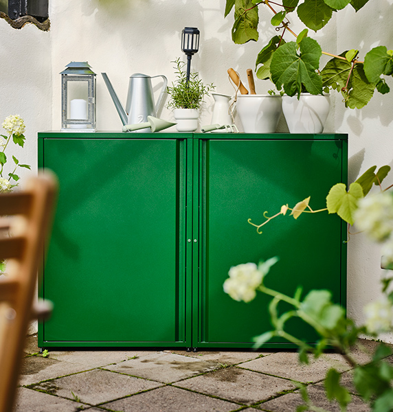Green outdoor cabinet with various items such as watering cans, pitchers and flower pots.