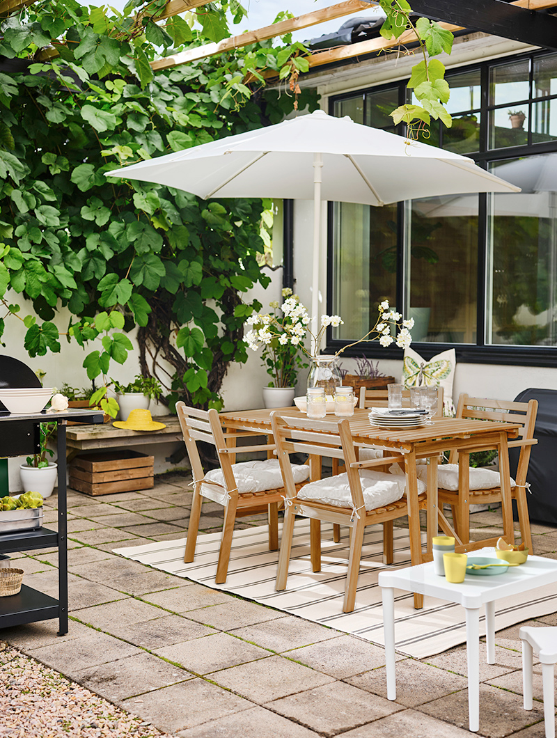 Barbecue area, with an outdoor table with 4 chairs, in front a small plastic dining area for children, in the background a barbecue and a closed parasol.