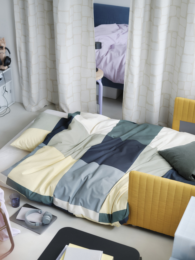 Studio apartment with a bed covered by a BRUNKRISSLA duvet, and LÖNNSTÄVMAL blackout curtains used as a room divider.
