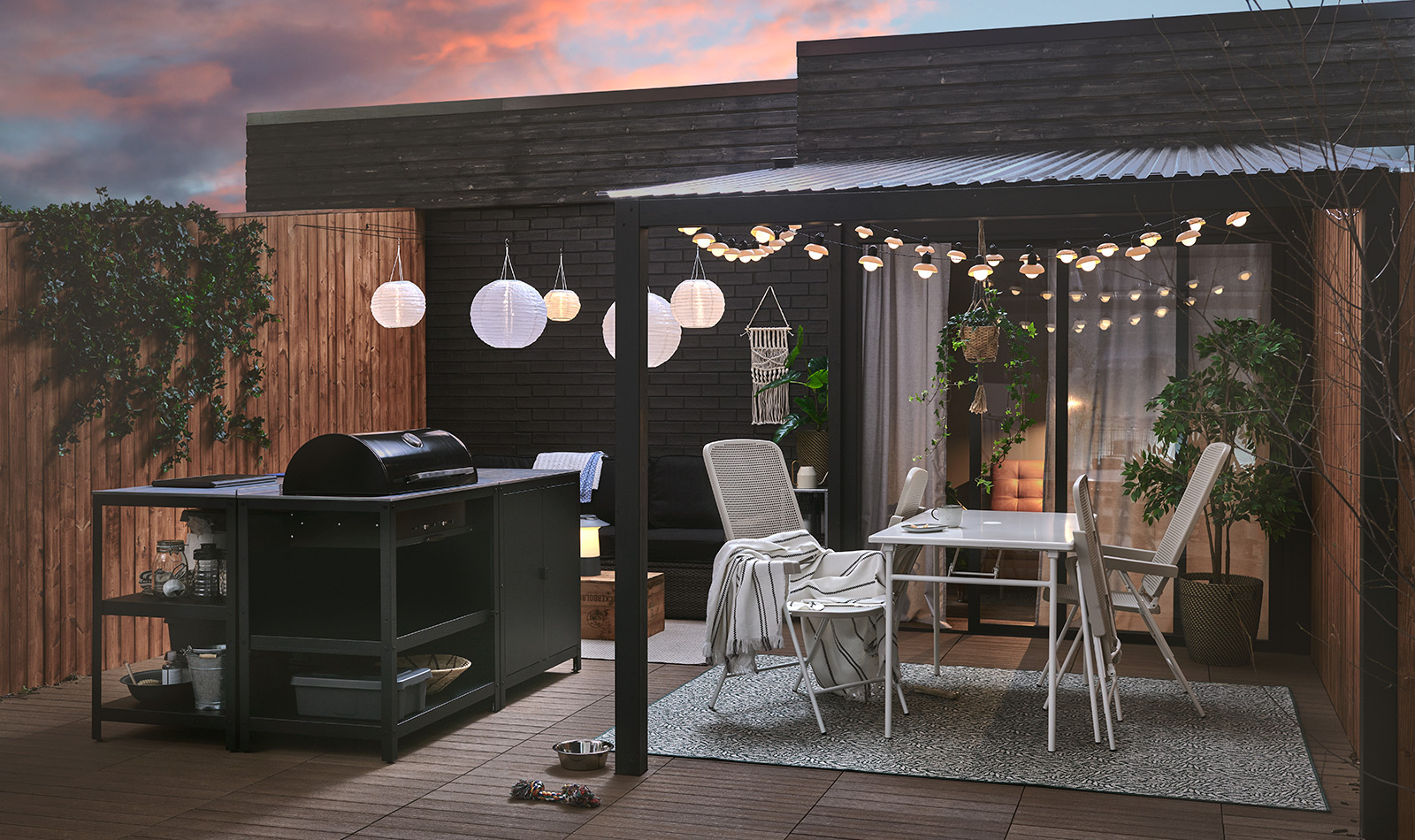 Patio oscuro con parrilla, comedor exterior y luces blancas colgantes. Crea un ambiente nocturno acogedor para reuniones al aire libre.